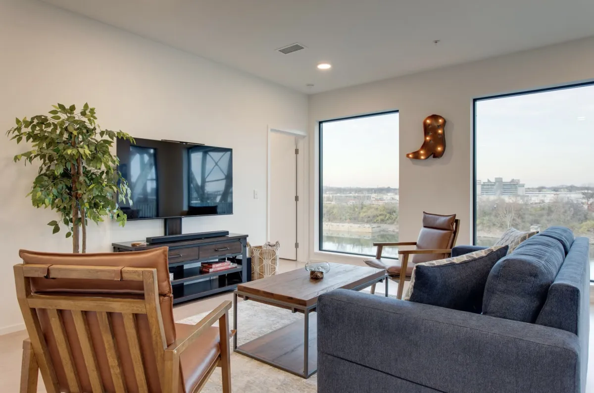 This interior shot features a stylish living area with large windows offering scenic views, a modern television, and thoughtfully arranged contemporary furniture. The windows suggest a strong connection to the outdoors and hint at the riverfront setting.