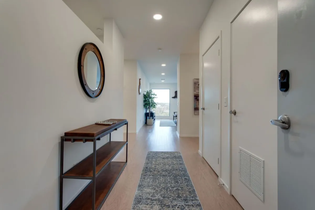 This image features a welcoming entryway with a wooden console table, mirror, runner rug, and a plant, creating an inviting atmosphere. The stylish décor hints at a space designed for gathering and making a good first impression as guests arrive.
