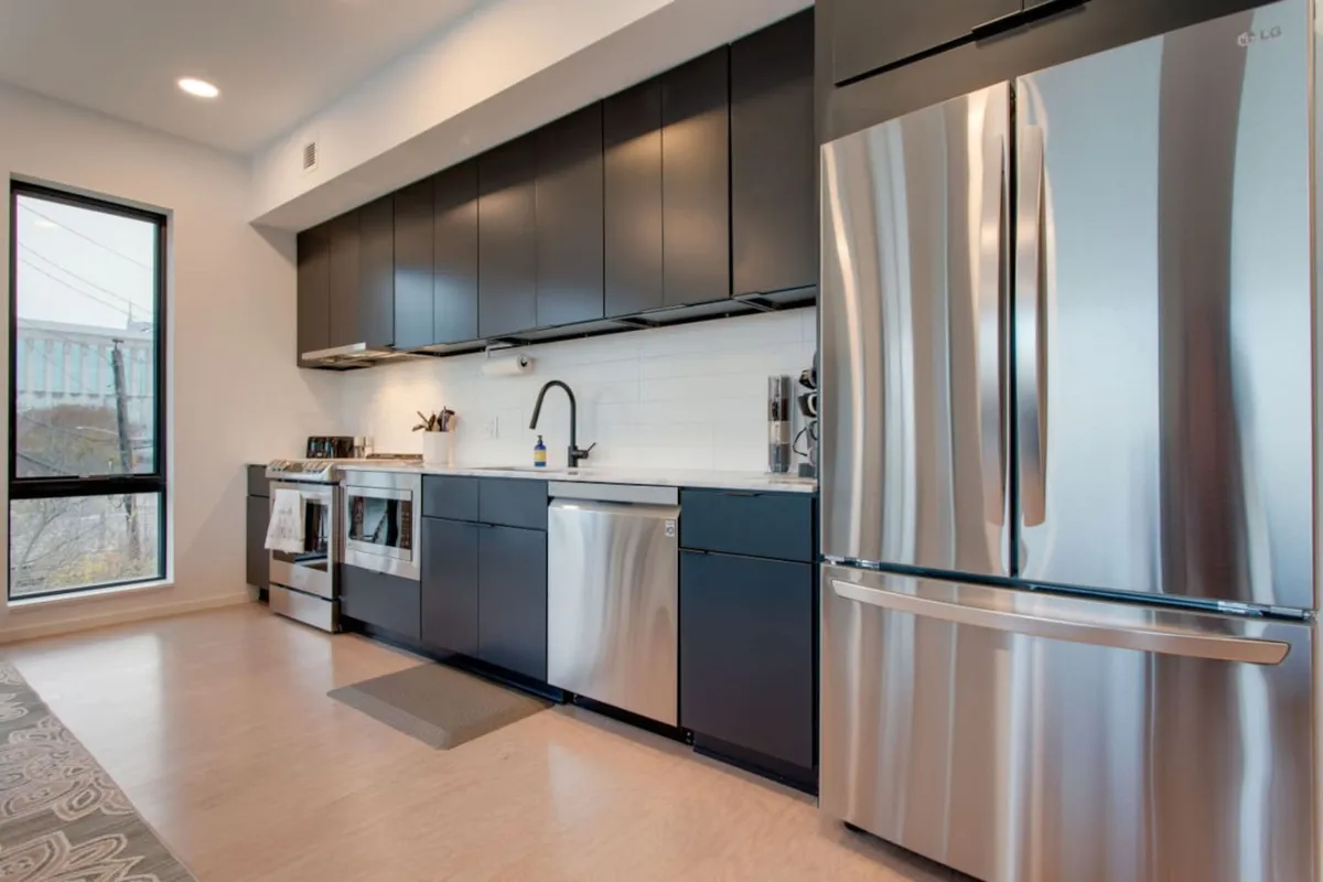 A contemporary kitchen with stainless steel appliances, black cabinetry, and a classic white subway tile backsplash. The design is clean yet inviting, with enough space to encourage group cooking or socializing over shared meals.