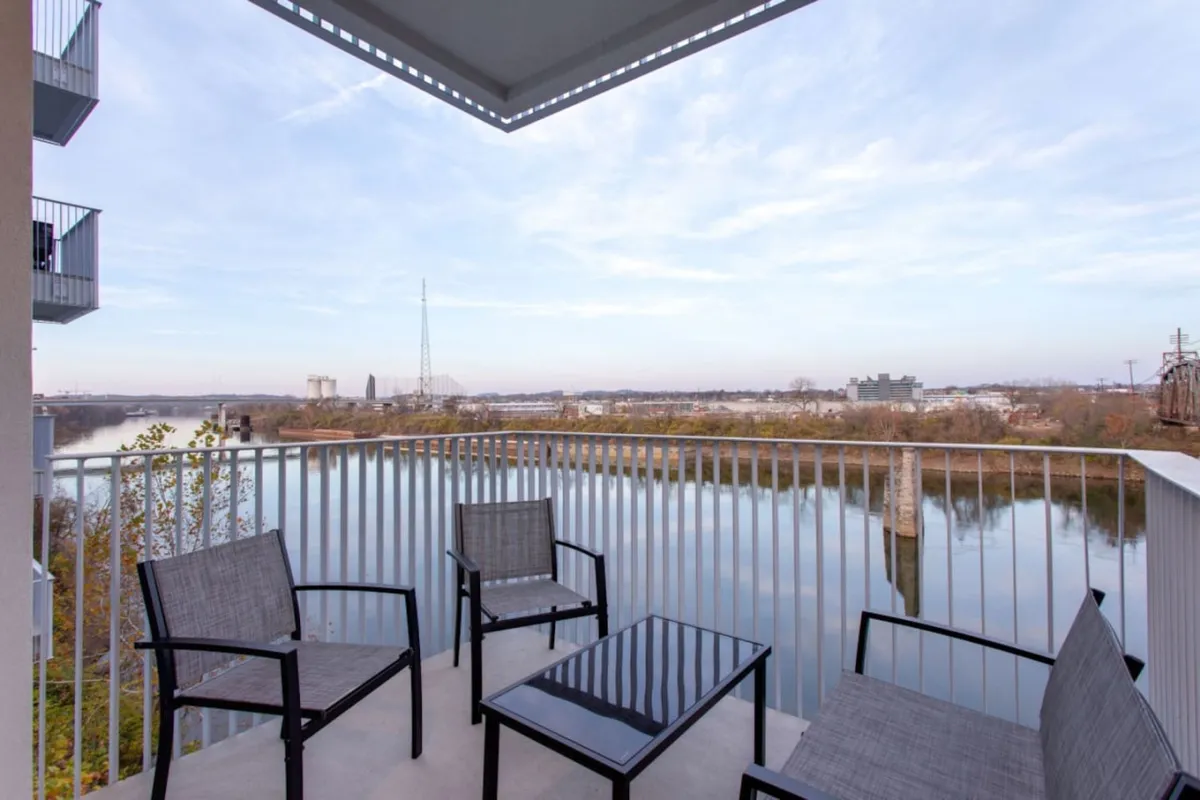 An outdoor scene featuring four comfortable chairs and a glass table on a balcony, overlooking the tranquil river. The arrangement is perfect for socializing or simply taking in the peaceful water views, with ample space for group hangouts or stargazing at night.