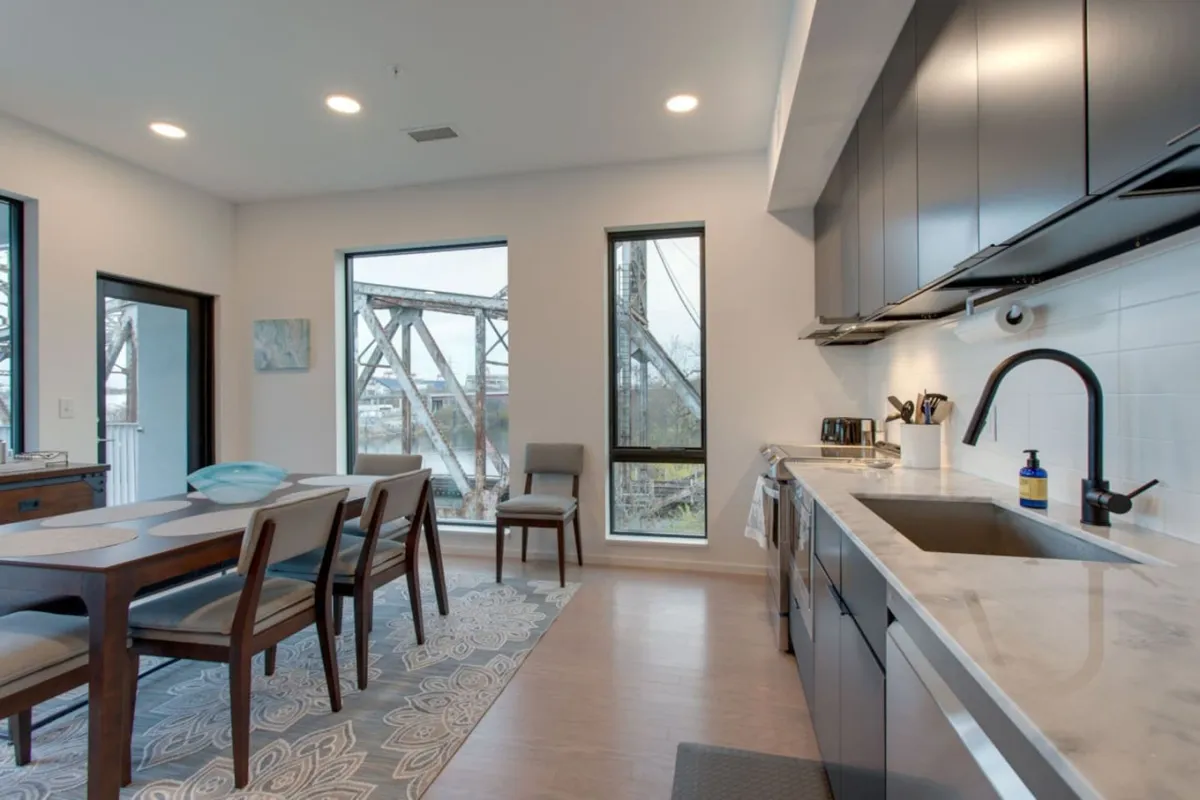 A dining space is shown with a table set near expansive windows, overlooking the outdoors and adjacent to a sleek kitchen counter. The scene conveys a relaxed, social environment ideal for morning coffee or hosting friends before or after city adventures.