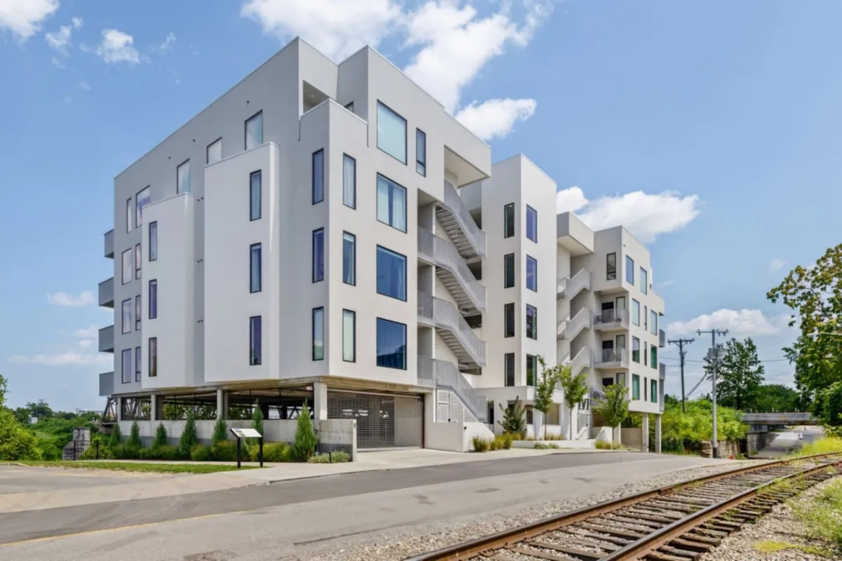 A contemporary exterior view of the building, showcasing modern architecture with expansive windows and prominent staircases. The image hints at the vibrant urban setting, with the structure situated amidst city life, inviting residents to step out and explore the neighborhood.