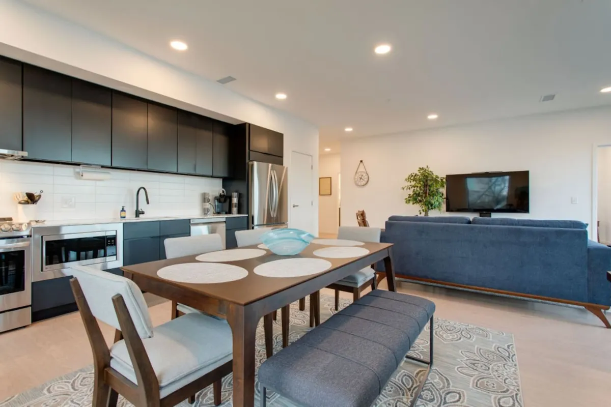 A modern, well-lit interior showing a dining table adjacent to a kitchen area, a comfortable living room couch, and a television—all arranged for easy social interaction and shared experiences.