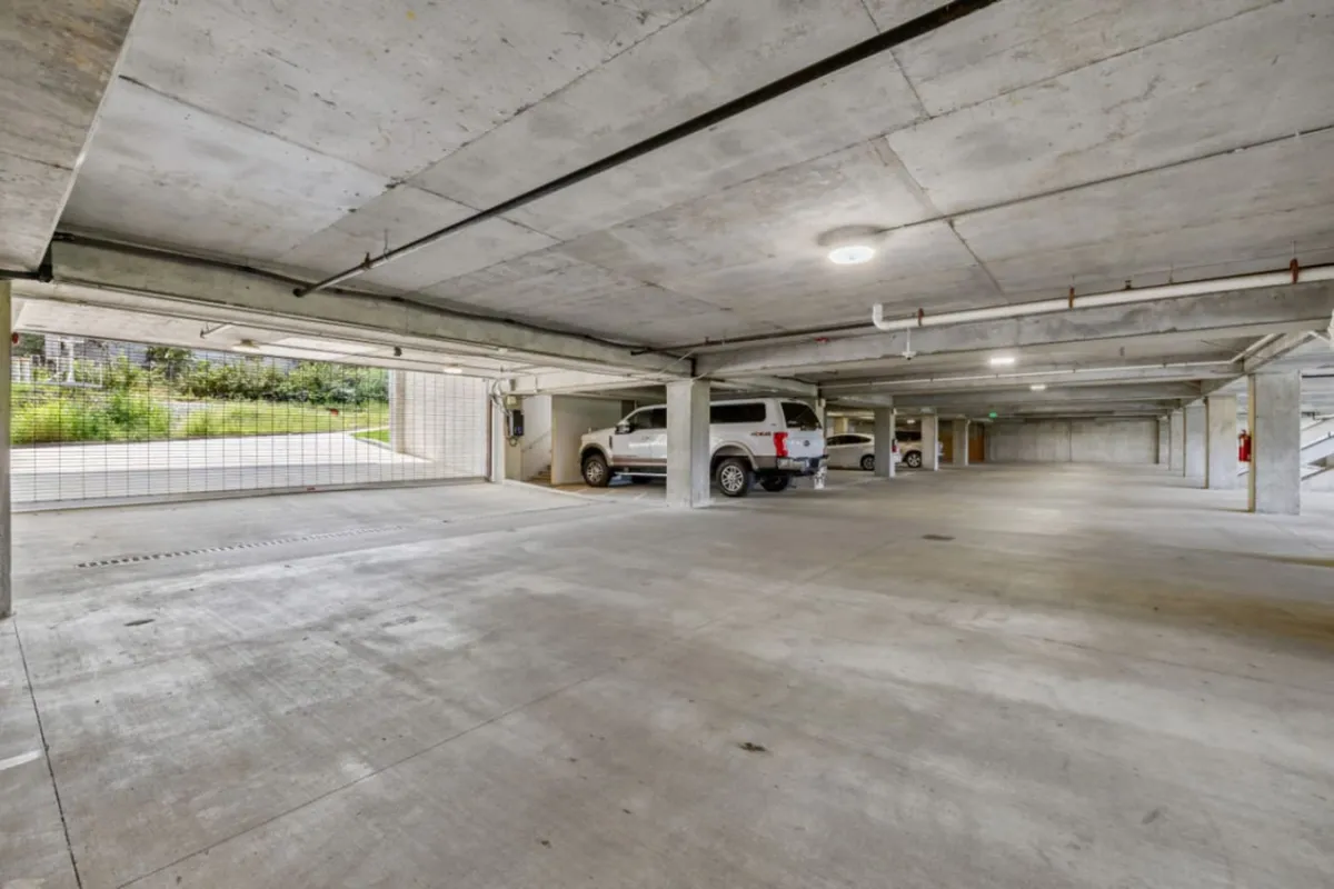 A functional view of the apartment's enclosed parking garage, featuring concrete pillars, parked vehicles, and generous open space. The image conveys secure, convenient parking for guests and residents alike.