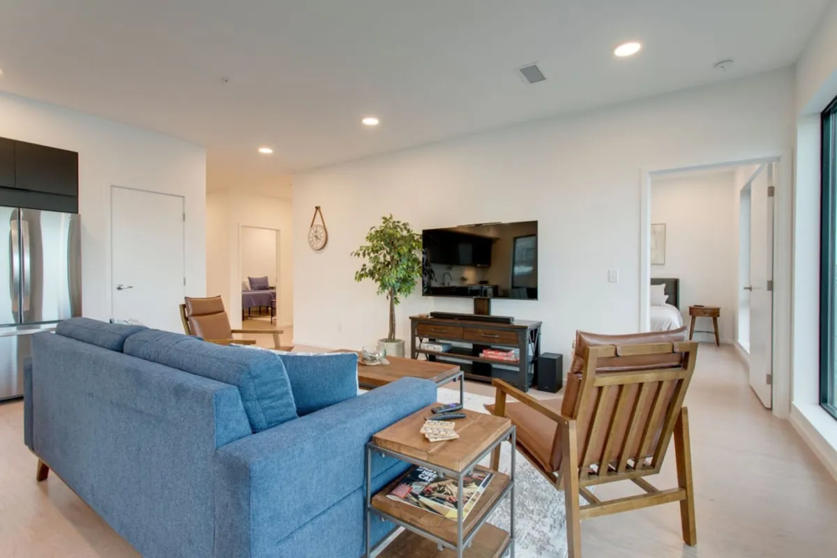 A cozy living room scene with a blue sofa, wooden coffee table, television, and indoor plant. The setup is perfect for socializing, relaxing, or watching pre- or post-game entertainment together.