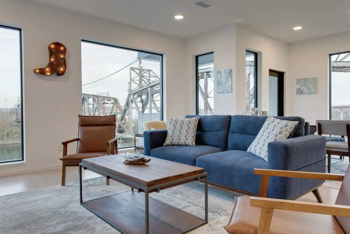 A modern, cozy living room featuring a stylish sofa, a wooden coffee table, large windows that flood the space with natural light, and tastefully chosen artwork on the walls. The scene invites socializing, relaxing, or enjoying a cup of coffee while watching the sunset.